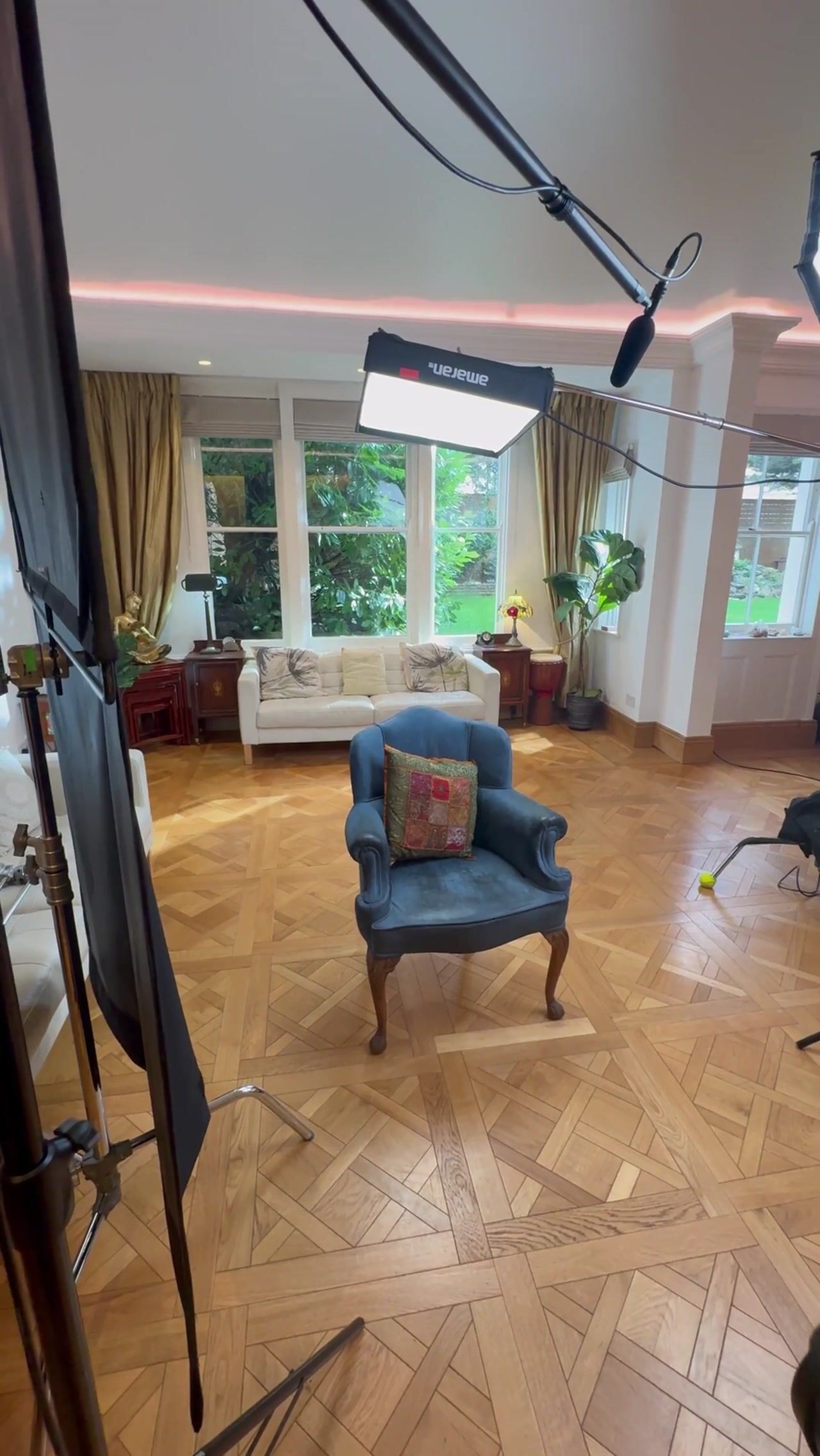 Empty blue armchair on parquet flooring in a lounge, rigged with an overhead panel light and boom microphone for an interview setup.